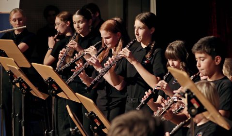 Holzbläsesektion eines Jugendorchesters im spielend im Stehen in schwarzen Konzertkleidern. Das Foto wurde schräg von der Seite gemacht.