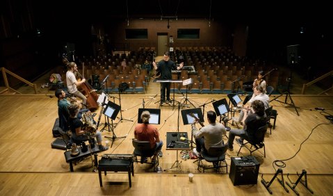 Ein Ensemble für neue Musik bei der Probe: auf verschiedensten Plätzen mit verschiedensten Instrumenten in einem Halbkreis.