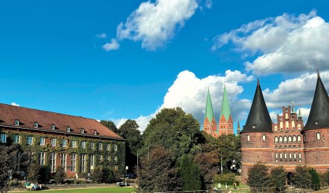 Die historische Stadtsilhouette von Lübeck: Prominent die Doppeltürme des Stadttores und die Doppeltürme der Marienkirche in der Ferne.