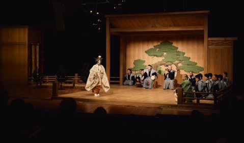B&uuml;hne mit traditionellem japanischen Theater, Darsteller*innen in Kost&uuml;men, Dekor mit bemaltem Baum.