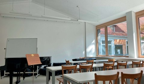 Ein leeres wie ein Klassenraum bestuhlter Raum mit einem Fl&uuml;gel vorne.