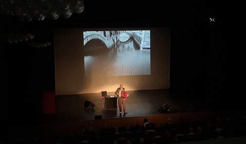 Bühnengeschehen: Ulrich Tukur mit Akkordeon. Im Hintergrund eine schwarzweiß-Stadtfotografie