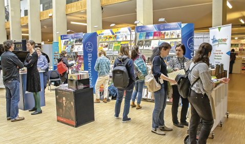 Eine Messestand-ähnliche Präsentation eines Musikverlags, mit einem dutzend interessierten Menschen.