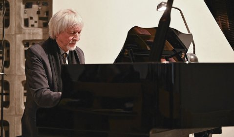 Gerhard Fischer-Münster, ein Mann mit weißen Haaren und Bart im dunklen Anzug, spielt einen Flügel.