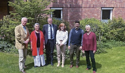 Die im Text genannten Personen stehen wie aufgelistet im Garten eines Backsteinbaus.