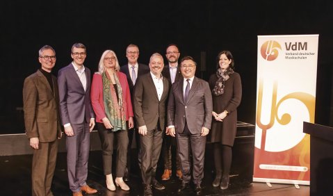 Der neue Bundesvorstand auf dunkler Bühne neben einem VdM-Transparent.