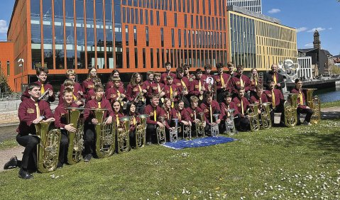 Die Brassband PotzBlech posiert einer Fußballmannschaft gleich in schwarz-weinroten Uniformen und Instrumenten vor dem Konserthus Malmö.
