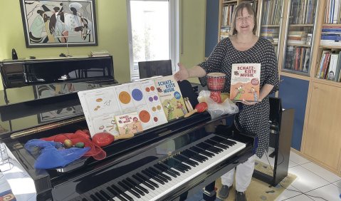 Frau Meyer steht ziwschen einem Flügel und einem E-Piano. Auf dem Klavier diverse Unterichtsmaterialien