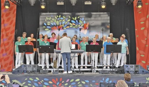 Eine Bühne, darauf ein Chor mit weißen Hosen und bunten Oberteilen
