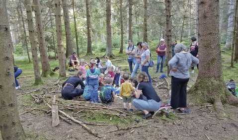 Eine Gruppe von Kindern und begleitende Erwachsene hocken im Wald.