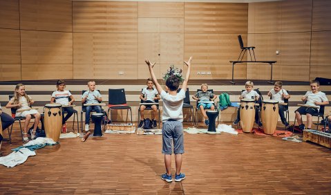 Ein kleiner Junge interagiert mit provisorischem Dirigat mit einer Trommelgruppe aus Gleichaltrigen.