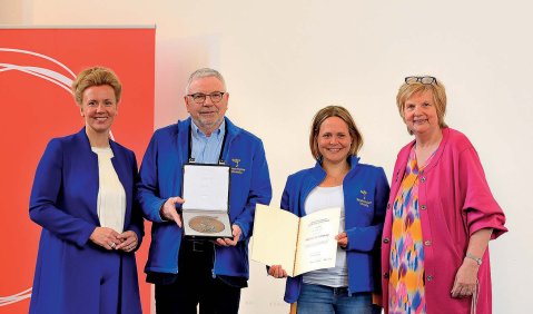 Vier Personen stehen zusammen und halten Dokumente und Plakette in die Kamera.