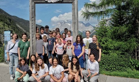 Eine Gruppe jugendlicher steht an einem steinernen Rahmen, der leer ist, druch den hindurch man aber ein entferntes Bergpanorama bestaunen kann.