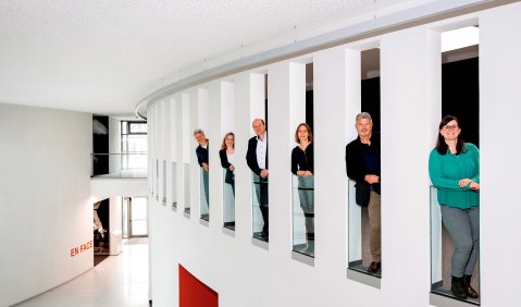 Die verschiedenen Personen stehen in Aussparungen im innern eines Gebäudes und schauen "heraus".