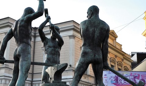 Ein Foto von der Statue "Drei Schmiede". Drei nackte Männer schmieden mit drei Hämmern auf einem Amboss.