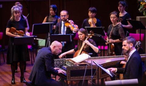 Ein eher rot beleuchtetes Barockensemble wird von einem glatzköpfigen Cembalisten geleitet.