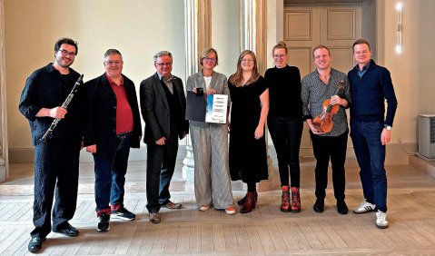 Die Gruppe aus 8 Menschen in einem steinernen Raum mit einer Galerie an Säulen.