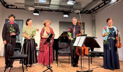 Fünf Musiker:innen in gedeckt-bunter Kleidung auf einer kleinen Bühne.