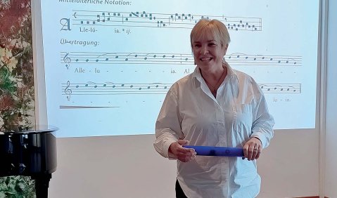 Ein Mann im höheren mittleren Alter vor einer Projektionsfläche mit mehreren Notenzeilen.