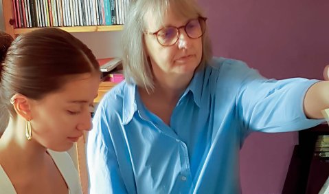 Eine Frau im mittleren Alter gibt einer jungen frau Klavierunterricht.