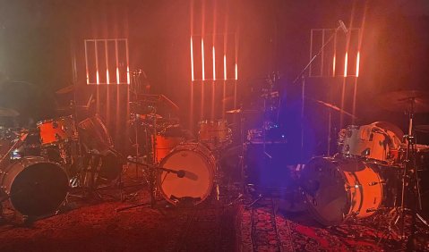 In schummrig rotem Licht stehen drei Drumsets.