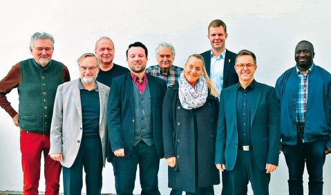 9 Personen verschiedener Geschlechter, Altersgruppen und Hautfarben stehen in einer Reihe zusammen.