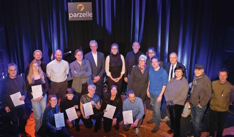 Gruppenfoto in einem dunklen Raum vor blauem Vorhang.