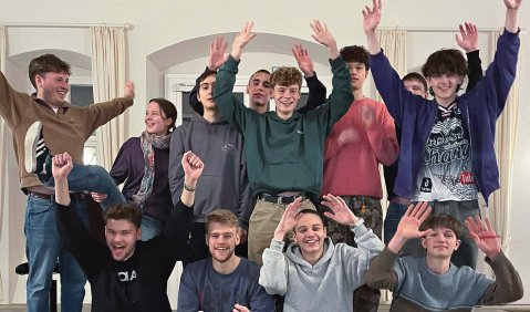 Eine kleine Gruppe von jungen Menschen posiert mit zum Jubel gestreckten Armen in einem Schlosssaal.