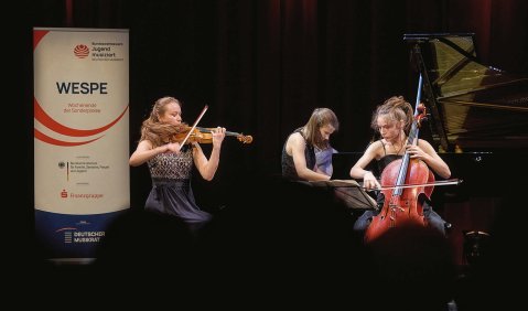 Ein Klaviertrio aus Jugendlichen spielt auf einer dunklen Bühne. Neben ihnen ein Aufziehtransparent: "WESPE" und Verbände- und Sponsorenlogos