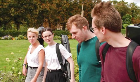 Vier junge Musiker:innen (ein Streichquartett) läuft durch einen Schlossgarten.