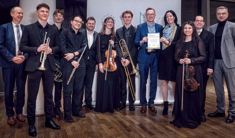 Einige junge Orchestermusiker:innen in Konzertmontur stehen zusammen mit sie flankierenden älteren Personen.