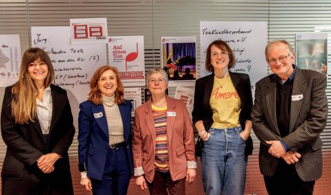Fünf Personen vor einer Wand mit mehreren Infoplakaten