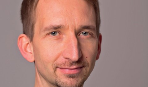 Ein Mann mittleren Alters mit kurzen blonden Haaren, einem l&auml;nglichen Gesicht, leichtem freundelichen L&auml;cheln, und einer relativ langen Nase.