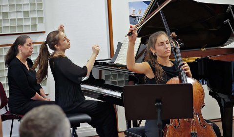 Zwei dunkelblonde junge Frauen – eine am Cello eine am Klavier – mit vom Schwung des Schlussklangs in die Luft gehaltenen Händen.