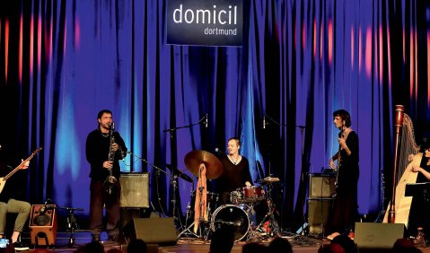 Eine Band mit Schlagzeug, Bassklarinette, Lauteninstrumenten und Harfe