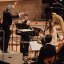 Dirigent mit erhobenen Armen vor einem Orchester, Musiker*innen spielen Instrumente wie Geige, Harfe und Fl&ouml;te. Foto: &copy; Berliner Festspiele, Fabian Schellhorn